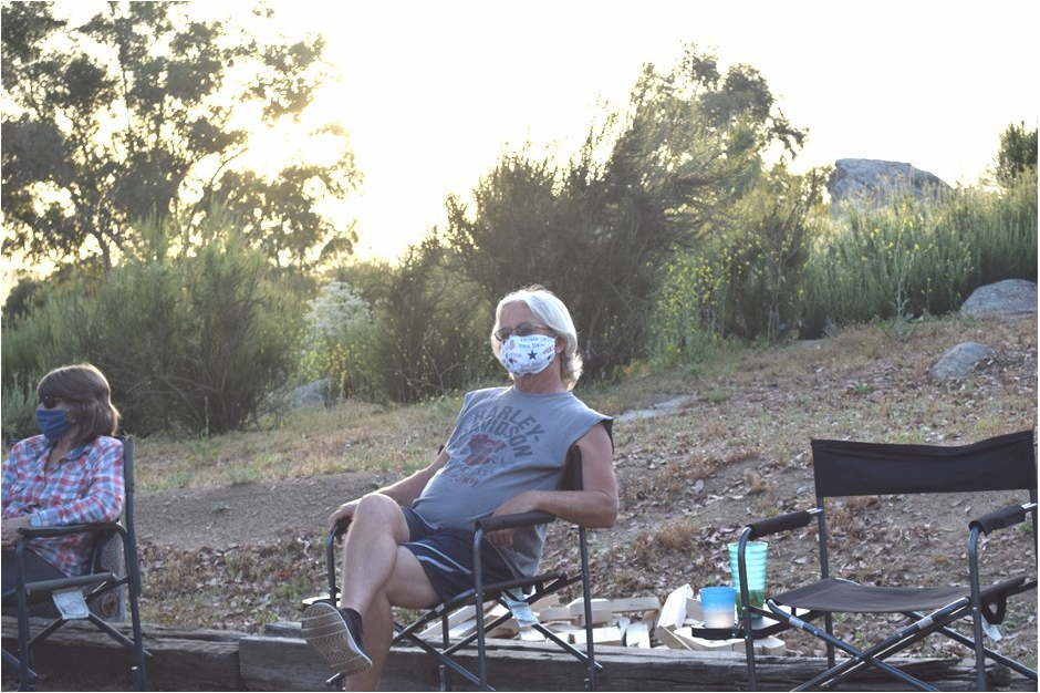 Two people sitting in camp chairs about six feet apart wearing masks.
